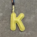 Buchstabe K Leder Taschenanhänger Detail Nahaufnahme mit gelbem Initial und Seidentuch. - K Hellgelb
