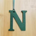 Close-up detail of dark green Epsom leather letter N charm bag pendant accessory. - Dark Green