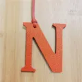 Close-up detail of orange leather letter N bag charm pendant showing textured surface and strap. - Orange
