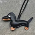 Gros plan détaillé du charm de sac en cuir de teckel mignon avec sa lanière noire élégante. - Noir