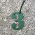 Close-up detail shot of a green textured number three leather bag charm with hanging cord. - Dark Green