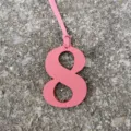 Close-up detail of the pink leather number 8 bag charm pendant, showing fine leather texture. - Pink