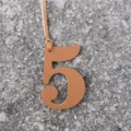 Vue de détail du pendentif de sac chiffre 5 en cuir marron avec lanière sur fond de pierre. - Marron