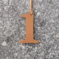 Detailed view of a number 1 leather bag charm in caramel color with textured finish. - Brown
