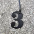 Close-up view of a black leather texture number three bag charm pendant detail shot texture. - Black