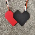 Detail shot of the dual-color leather heart bag charm with silk ribbon strap texture close-up. - Black and Red