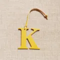 Close-up detail view of yellow leather letter K bag charm with thin strap accessory. - Yellow