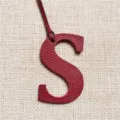 Nahaufnahme des roten Leder Buchstaben S Taschenanhängers mit feiner Textur und Aufhängeband. - Burgunderrot