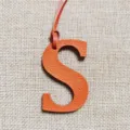 Nahaufnahme des orangefarbenen Leder Buchstabens S Taschenanhängers mit feiner Textur. - Orange