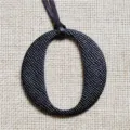 Close up detail view of a black textured leather letter O bag charm fashion accessory - Black
