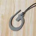Detailed close-up shot of the grey textured leather bag charm pendant hanging on a wooden surface. - Gray
