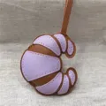 Vista dettagliata di un grazioso ciondolo in pelle a forma di croissant per borsa. - Viola chiaro