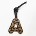 Close-up detail of leopard print leather letter A bag charm with black strap and neat stitching. - Letter A