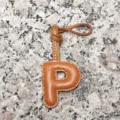 Close-up of light brown leather letter P bag charm showing neat stitching and loop strap. - Letter P / Tan