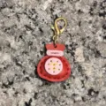 Detailed close-up of the handmade red leather lucky bag keychain charm with gold clasp. - Red