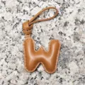 Close-up detail of a light brown leather puffy letter W bag charm with contrast stitching. - Letter W / Tan