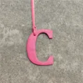Pink leather letter C bag charm detail shot showing the textured finish and thin strap. - Rose Red