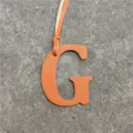 Detailed view of the orange leather letter G bag charm with dual straps and fine texture. - Orange