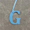 Close-up detail of light blue leather letter G bag charm with hanging strap, stylish accessory. - Sky Blue