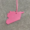 Detailed close-up of a pink leather map shaped bag charm pendant with matching strap. - Rose Red