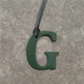 Green leather letter G bag charm detail, textured leather monogram pendant with hanging cord. - Dark Green