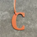 Orange leather letter C bag charm, detailed closeup showing fine textured leather finish and strap. - Orange