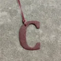 Close-up detail of a burgundy leather letter C bag charm pendant with a hanging strap. - Burgundy