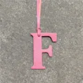 Detailed close-up of pink leather letter F bag charm showing fine textured grain and strap. - Pink