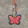 Detalle de primer plano del dije de bolso de mariposa de cuero con correa de pañuelo de seda. - Rojo Y Negro