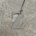 Detalle de dije de bolsa letra Z de cuero gris, elegante accesorio con correa colgante. - Gris