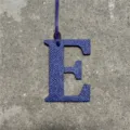 Close-up of blue textured leather letter E bag charm, showing delicate leather grain and stitching detail. - Sapphire Blue