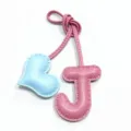 Vista di dettaglio del ciondolo borsa lettera J in pelle rosa e cuore azzurro con cuciture. - Lettera J con Ciondolo a Cuore / Rosa e Blu chiaro