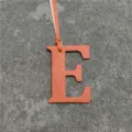 Orange leather letter E bag charm detail view, stylish handbag pendant accessory. - Orange