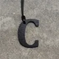 Close-up view of black leather letter C bag charm pendant accessory showcasing fine texture. - Black