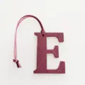 Leather letter E bag charm detail view, exquisite burgundy leather texture with hanging strap. - Burgundy