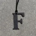 Detailed close-up view of a black textured leather letter F charm hanging on a cord. - Black