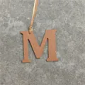 Close-up detail of luxury leather M letter charm pendant, textured tan leather material. - Brown
