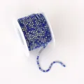 Primer plano de cadena de pedrería azul en carrete, ideal para manualidades y detalles de ropa. - Mezcla de strass azul real con base a juego