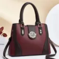 Close-up detail of the stylish maroon and brown leather handbag with golden hardware deco. - Red