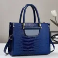 Close-up van de glanzende blauwe krokodillenpatroon handtas met fijne textuur en metalen hardware. - Blauw
