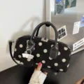 Close-up detail of the chic black and white polka dot handbag, featuring dual handles & charm. - Black