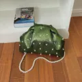 Detailed view of green glossy shell evening bag with pearl embellishments and beaded chain. - Green