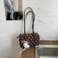 Detalle de bolso de boliche de lunares marrón con textura de tela, cremallera y abalorio. - Café con Colgante