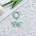 Detailopname van de lichtgroene strik sleutelhanger hanger, toont glanzende textuur en metalen ring. - Groene strik met veergesp