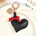 Zwarte leren hart sleutelhanger met rode strik en gouden ring, stijlvolle tasaccessoire. - Zwart Leren Hart / Zwart