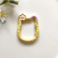 Gedetailleerde close-up van de schattige katvormige legering veersluiting met bloemen-emailledecoratie. - Geel
