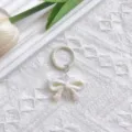 White pearlescent UV bow keychain charm, detailed close-up shot on white lace background. - Beige Bowknot & Spring Ring Clasp