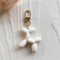 Close up of a cute white rubber balloon dog keychain with gold clasp detail product shot. - White