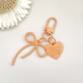 Close-up detail van een mooie perzikroze legering strik sleutelhanger met hart hanger. - Oranje veersluiting met legering strik en hartbedeltje