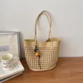 Nahaufnahme der beigen gewebten Loch-Tasche mit Henkeln und Blumen-Anhänger auf Holztisch. - Mit Anhänger / Gelb